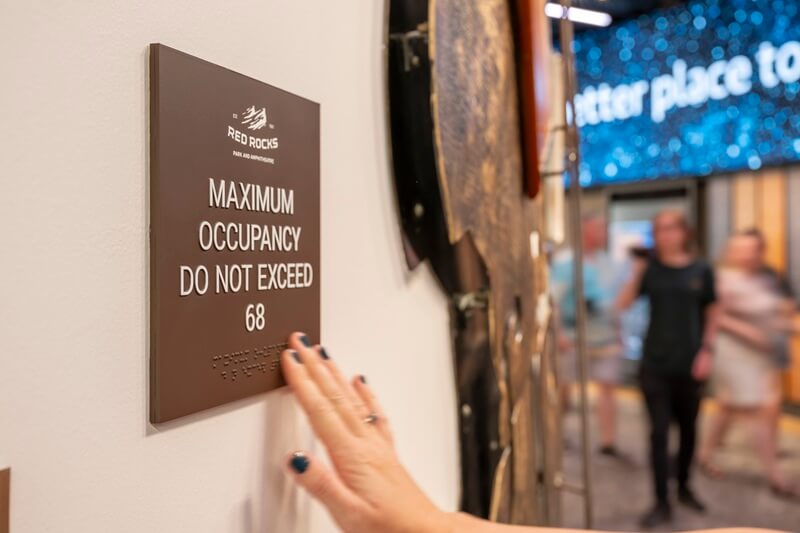 An image of someone touching the braille on a Maximum Occupancy sign,